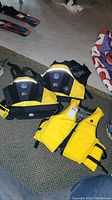 Three yellow adult life jackets on a carpet, two larger and one smaller, showing front and side views with adjustable straps and zippers