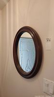 Side view of oval mirror showing rounded cherry wood frame and partial reflection of glass door with decorative textured glass.