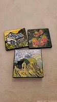Overview of three small square paintings: one house with yellow, one floral, one house with hills and flowers