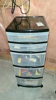 Full view of plastic storage tower with five semi-transparent drawers and black top