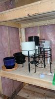 Photo showing metal plant stands, two ceramic pots with bases and several plastic pots on wooden shelving.