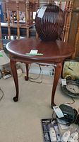 Front view of round cherry wood end table with a lamp on top and surrounding items.