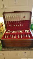 Full view of the open wooden canteen displaying the silver-plate flatware set arranged in red velvet lining with slots for each piece.