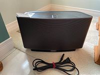 Front angle of black Sonos Play:5 wireless speaker showing metal mesh and power cable.