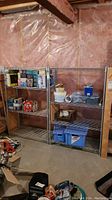 Two metal wire storage shelves side by side, partially filled with various household items, in a basement with pink insulation.