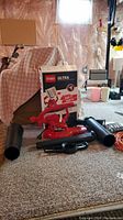 Toro Ultra electric leaf blower with original box, three black nozzle attachments, and orange extension cord arranged on carpeted floor in basement setting.