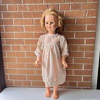 Full front view of the 34 inch Patti Playpal size doll standing in front of a brick wall, wearing a white dress.
