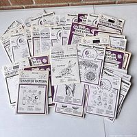 Photo showing a spread of over 50 sealed embroidery iron-on transfer pattern packets with various designs mostly from Walker's transfer pattern series.