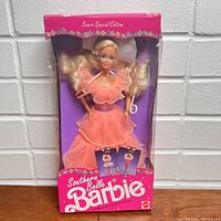 Frontal view of the Mattel Southern Belle Barbie doll in original pink packaging, showing the doll in peach layered ruffle gown with a purple belt and attached pink bow tie and blonde hair.