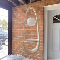 Front view of lamp suspended by chain against brick backdrop showing full teardrop frame, shelf and globe.