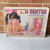 Box showing vintage Sears Health Center Barbie Doll playset branding and age recommendation (4 and up). Box shows wear and surface scuffing.