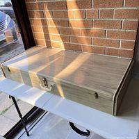 Closed view of the vintage metal under the bed box showing rectangular shape with wood grain finish and lock on the front.