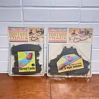Front view of two unopened packages of Motorific Torture Track accessories, one with 6 curved track pieces and the other with left and right track switches.