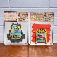 Front view of two Motorific Torture Track Accessories packages: one with 'Y' switches, one with shock absorber test sign and red track pieces.