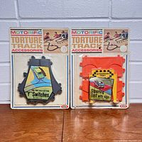 Front view of two Motorific Torture Track accessories in original packaging, showing 'Y' Switches and Steering Test with Sign items.