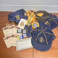 Photo showing scout uniform items including cap, shirt, neckerchief, belt, badges, and various certificates and pins laid on table.