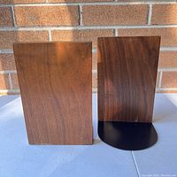 Front view of two vintage teak wood bookends with black metal bases against a brick background.