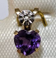 Close-up of 10K gold pendant with heart-shaped amethyst and small diamond accent showing prong setting and decorative bezel