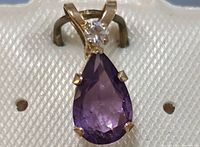 Close-up of 10K yellow gold pendant with pear-shaped purple amethyst and small clear stone above it.