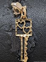 Close-up front view of 10K yellow gold key-shaped pendant with two heart cutouts in the bow, showing polished gold surface and bail.