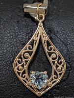 Close-up photo showing 10K gold pendant's filigree design with heart-shaped blue topaz stone centrally placed.