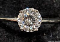 Close-up of the round brilliant cut moissanite stone in a 10K gold band from an angled top view.