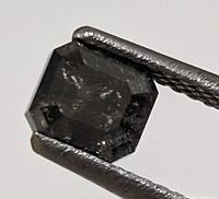 Close-up of the black diamond held by tweezers showing the emerald cut shape and internal characteristics.