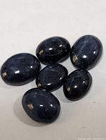 Six oval cabochon cut dark blue star sapphires displayed on a white background.