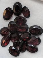 Close-up image showing a cluster of dark reddish-brown oval faceted garnet gemstones placed inside a white tray.