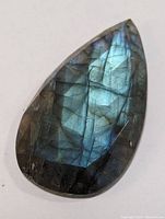 Top view of pear-shaped polished labradorite showing blue-green iridescence and faceted surface.
