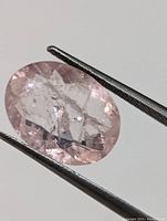 Close-up view of the oval cut pale pink genuine morganite gemstone held by tweezers.