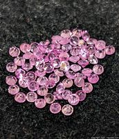 Pile of small round pink sapphire gemstones on black background