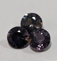 Three round cut sapphires showing color change properties from dark to light purple/black tones.