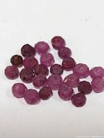 Close-up photo of approximately 28 faceted natural ruby beads in varying shades of red and pinkish hues, all drilled for jewelry use.