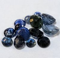 Multiple faceted loose sapphire gemstones in various blue and greenish shades, showing different cuts and sizes.