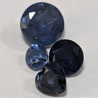 Four loose sapphires: including large round, small round, dark round and heart-shaped stones showing deep blue color and faceting.