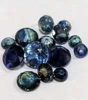 Loose genuine sapphire gemstones of varying blue shades, cuts, and sizes laid out on white background