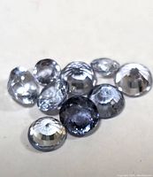 Ten round faceted tanzanite gemstones of varying light to medium blue and bluish-purple shades arranged on a white surface.