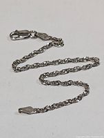 Silver 7 inch rope chain bracelet with lobster clasp shown laid flat on white background. Close-up of the chain links and clasp, highlighting the 925 sterling silver stamp on the clasp.