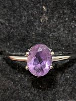 Clear close-up of sterling silver ring with oval faceted purple amethyst gemstone against black background.