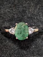 Close-up frontal view of sterling silver ring with emerald center stone and two clear side stones.