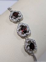 Close-up showing three linked silver segments each with an oval garnet surrounded by cubic zirconia stones in flower-shaped settings.