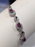 Close-up view of portion of sterling silver bracelet highlighting oval ruby set in a round bezel surrounded by small cubic zirconia stones, with infinity symbol accents.