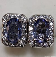 Close-up of the front face of both earrings showing tanzanite stones surrounded by cubic zirconia in sterling silver setting.