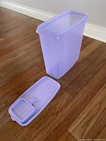 Tall lavender rectangular cereal/flour container open with lid placed beside it on wooden floor.