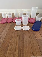 Nine assorted Tupperware containers with various lids arranged in rows on wooden floor.