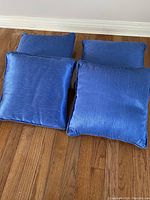 Four blue square cushions placed on a wooden floor showing fabric texture and color.