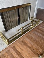 Rectangular brass fireplace fender placed in front of a fireplace hearth with marble or stone surround. Shows overall good condition and polished brass finish.