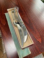 Two metal carving shears placed in their original box on a wooden surface with a protective cloth underneath.