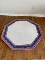 Custom octagonal carpet laid flat on wooden floor, showing its white center with purple, blue wavy line and pinkish border edges.